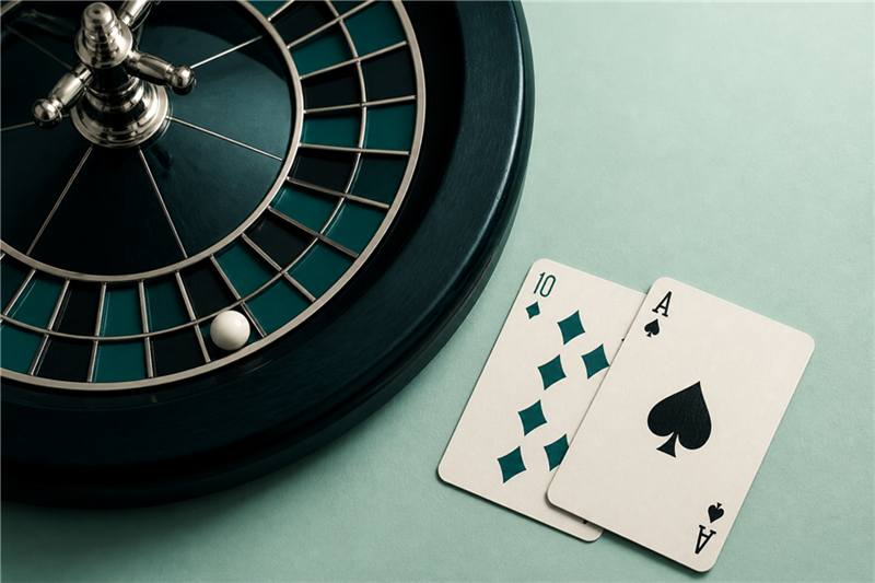 Roulette wheel detail and playing cards on a mint surface